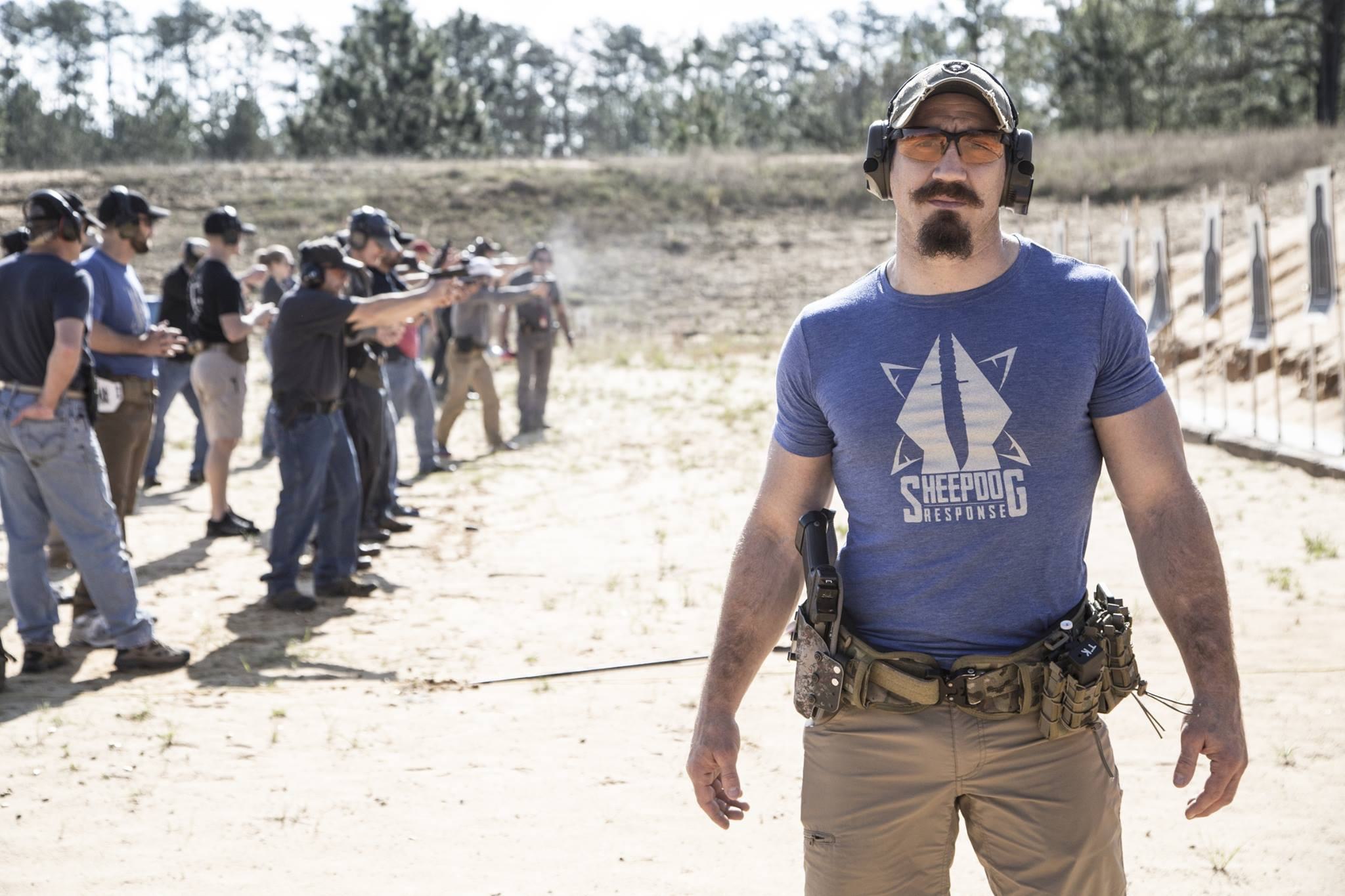man poses with shooting practice in background